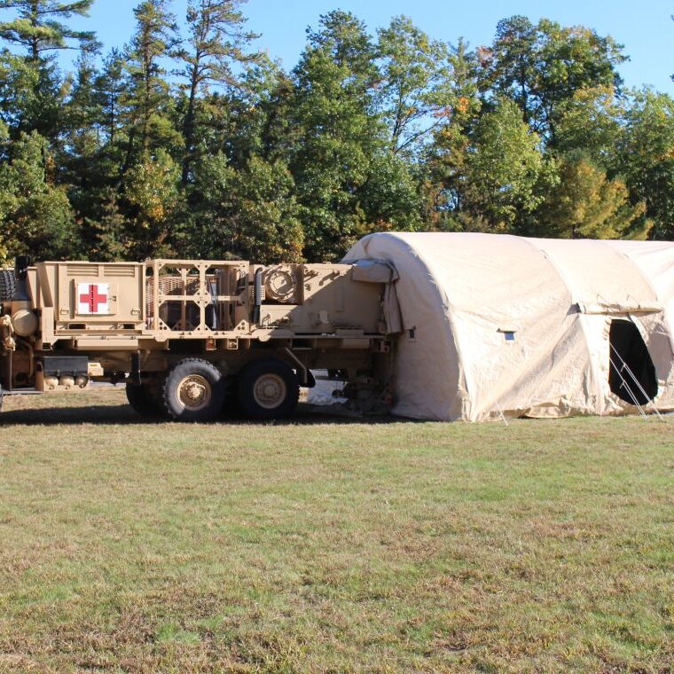 Custom tan medical shelter made of CBRN materials attached to truck.