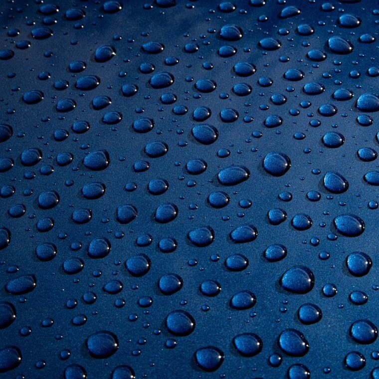 Hydrophobic films on dark blue material with water droplets.