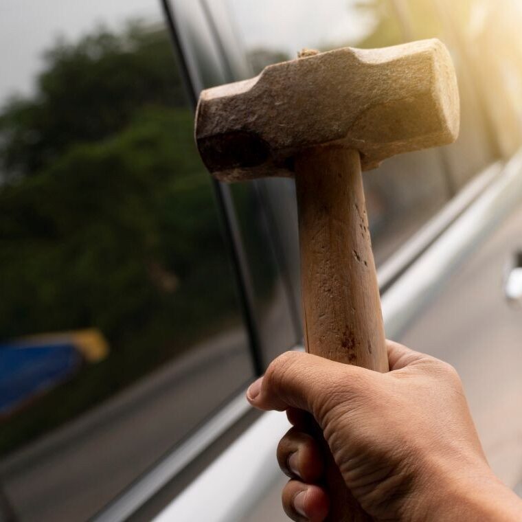 Hammer about to hit car driver's side window reinforced by safety glazing film.